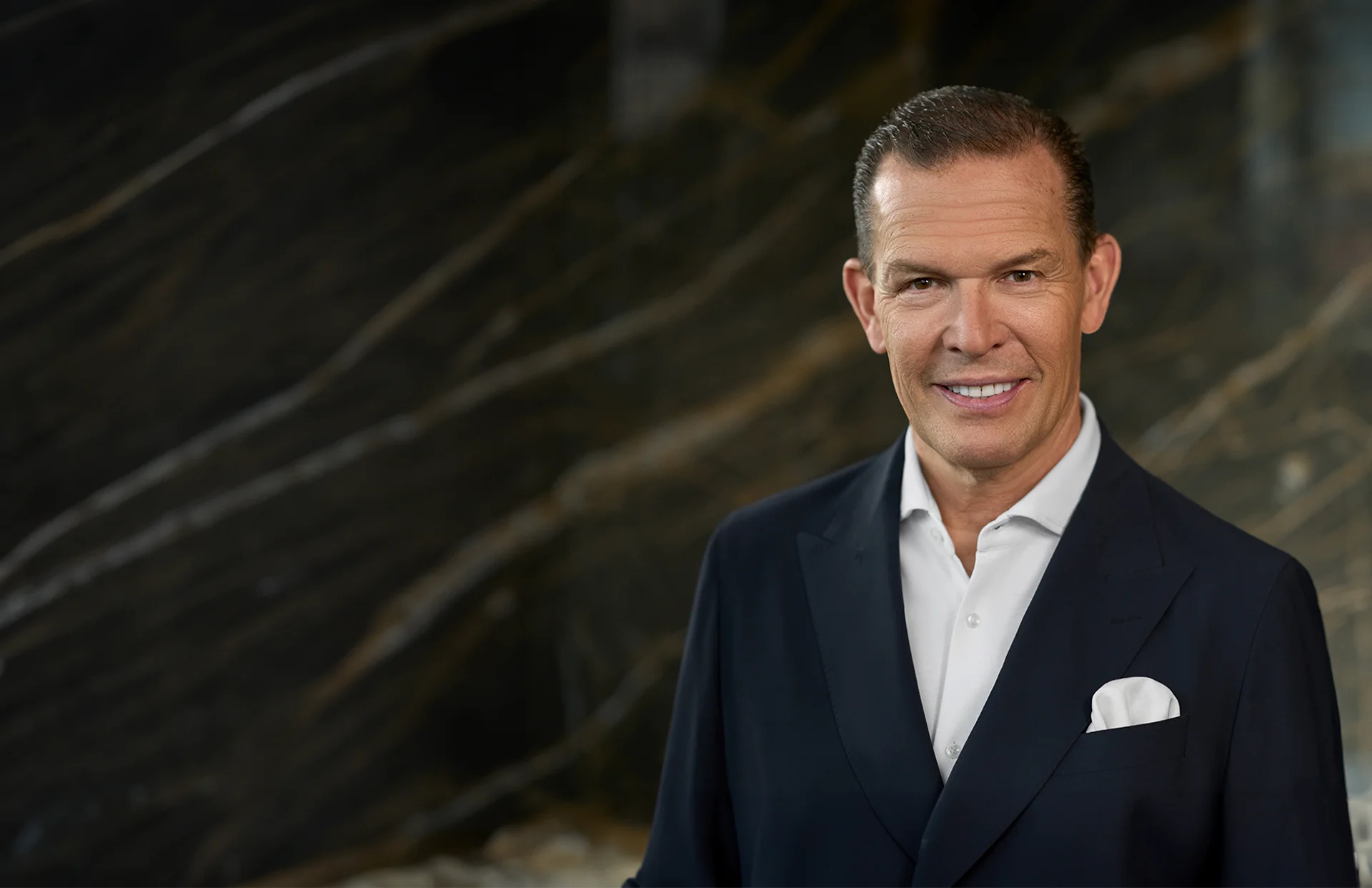 Daniel Grieder in a camel-colored suit against a dark background (Photo)